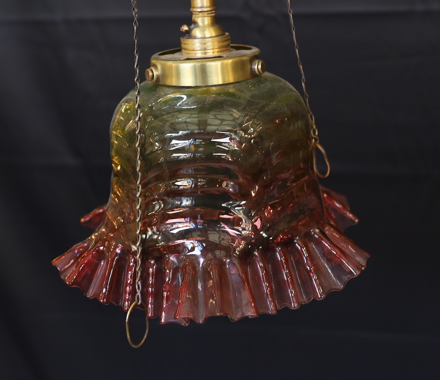 A 1920s English brass gasolier ceiling light with ruby tinted frilled glass shade, converted to electricity, height 76cm